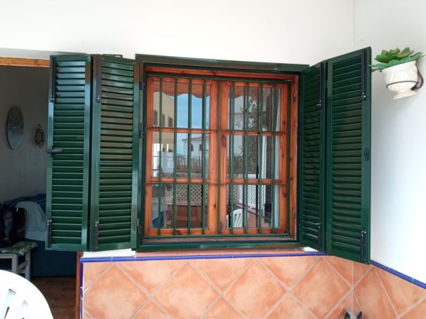 Ventana con contraventanas verdes y reja, enmarcada por azulejos en un ambiente interior.