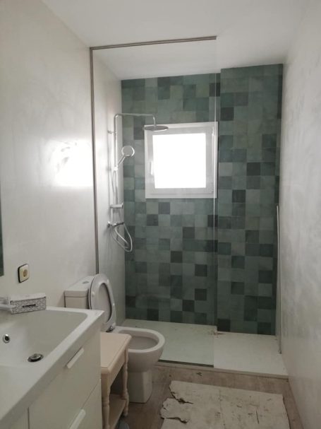 Baño moderno con ducha de cristal, lavabo y retrete en tonos verdes.