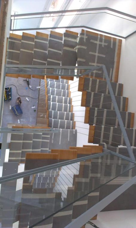 Escaleras modernas con peldaños de madera y barandilla de cristal, vista desde arriba.