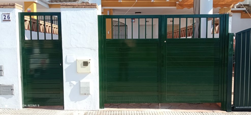 Puerta verde de acceso con una entrada lateral más pequeña a la izquierda.